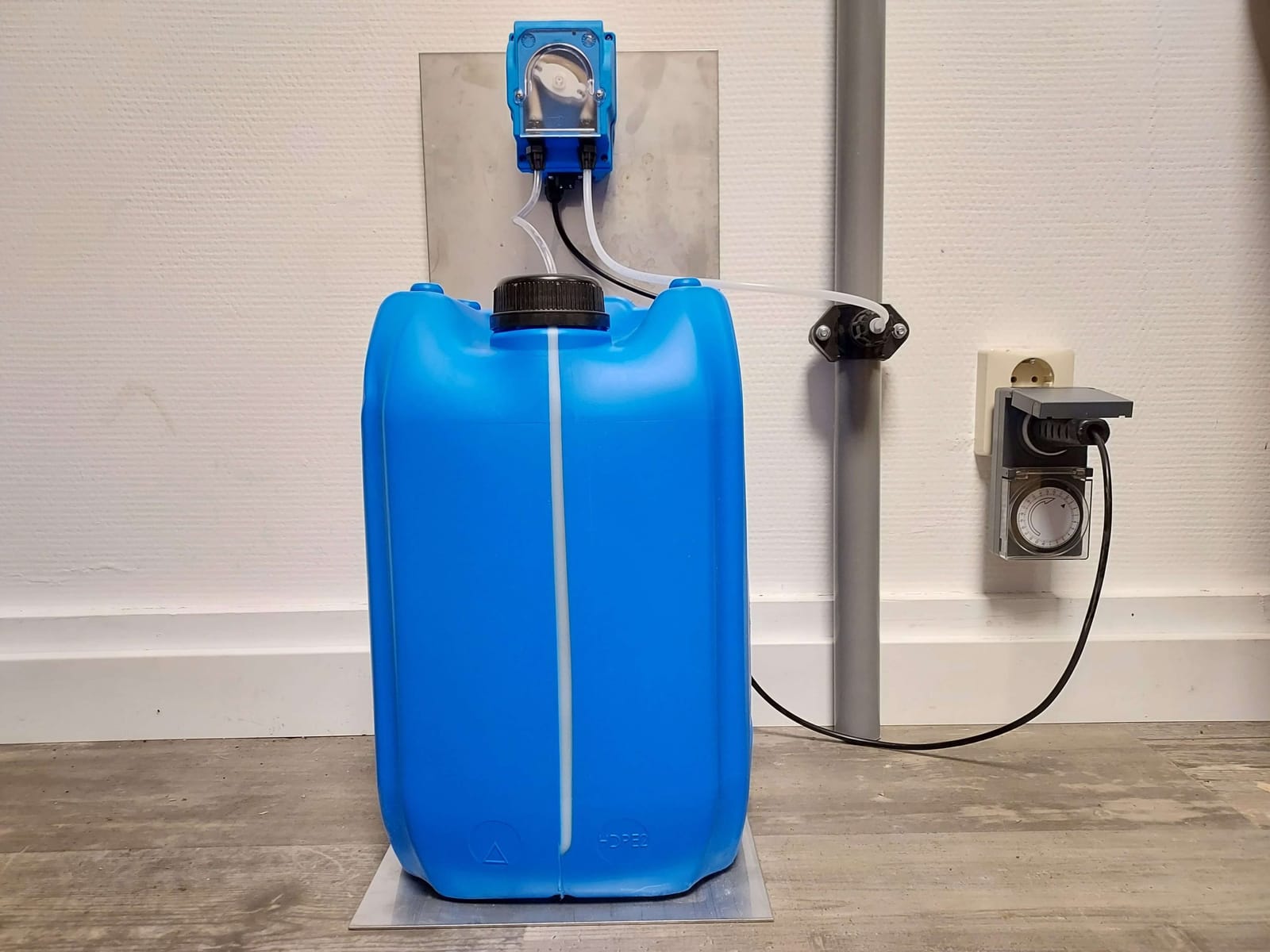 Greasy doseersysteem: blauw vat van 20 liter met doseerpomp en timer aan de muur